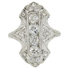 This incredible, all original, antique Edwardian period ring by Lambert Bros. is crafted in solid platinum. The ring showcases 16 old European & single cut diamonds elegantly pave set across the long and unusual design. The fiery diamonds in this antique ring total approximately 1 carats in weight, and display spectacular amount of brilliance that reflects their very fine quality. The magnificent floral pattern etching, milgrain and open filigree work is evidence of what phenomenal workmanship w Luxury Antique Diamond Ring With Single Diamond, Luxury Antique Filigree Ring With Diamond Cut, Luxury Antique Filigree Ring Collectible, Antique Silver Filigree Diamond Ring, Antique Diamond Filigree Ring Collectible, Antique Cocktail Ring, Unusual Design, 1 Carat, Antique Rings