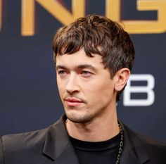 a close up of a person wearing a black shirt and suit with a chain around his neck