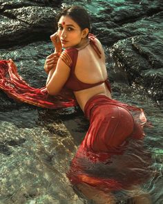 a woman is sitting in the water with her hand on her face and wearing a red sari