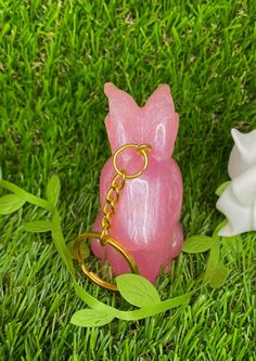 a pink pig keychain sitting on top of grass next to a white flower