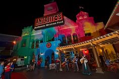 the entrance to an amusement park at night with people standing outside and playing instruments in front