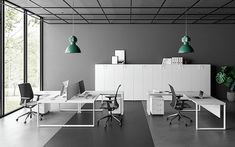 an empty office with two desks and green lamps hanging from the ceiling above them