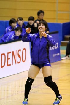 a female volleyball player on the court with her arms out and hands in the air