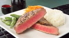 a white plate topped with meat and rice next to green beans on top of a table