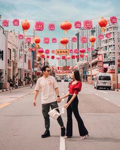 a man and woman holding hands in the middle of an empty street with chinese lanterns overhead