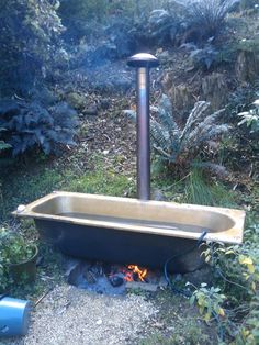 an outdoor fire pit in the middle of some bushes and trees with a metal pole sticking out of it