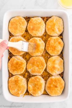 a hand holding a brush in a casserole dish with meat and cheese on top