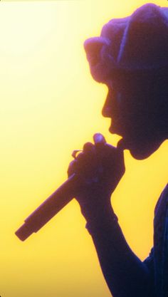 the silhouette of a person holding a microphone in front of an orange sky at sunset