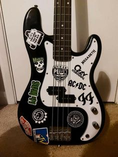 a black and white bass guitar with stickers on it's body, in front of a door