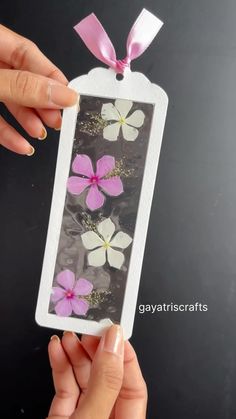 a hand holding a tag with pink and white flowers on it in front of a black background