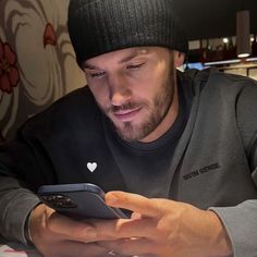 a man sitting at a table looking at his cell phone while wearing a beanie