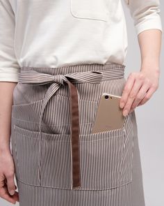 a woman wearing an apron and holding a cell phone in her hand with a pocket