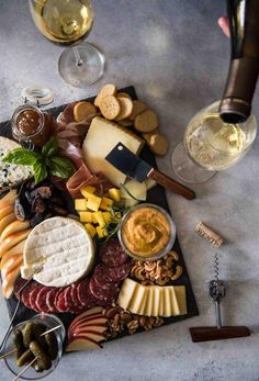 an assortment of cheeses, crackers, and wine on a slate platter