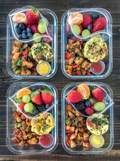 four plastic containers filled with different types of food on top of a wooden table next to oranges, strawberries and grapes