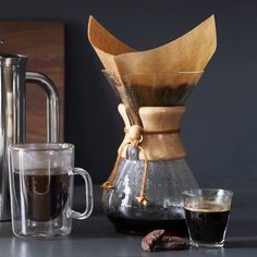 a coffee pot and two cups on a table next to a metal carafe with a wooden handle