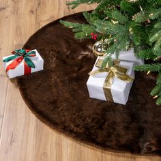 two wrapped presents under a christmas tree on a brown area rug with gold and green bows