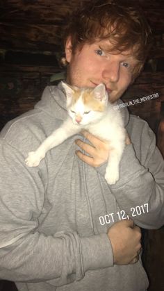 a man holding a white and orange cat in his arms while wearing a gray hoodie