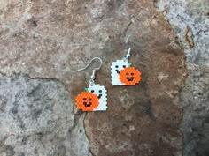 a pair of orange and white beaded pumpkin earrings on top of a rocky surface