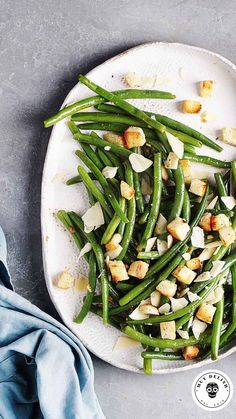 a white plate topped with green beans and croutons next to a blue napkin