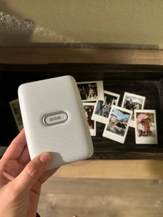 a hand holding an electronic device in front of a table with pictures on it and a wooden shelf