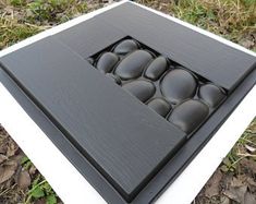 a black and white box with rocks in it on the ground next to some leaves