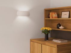 a wooden desk with flowers and pictures on the top shelf next to a wall light