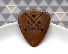 a wooden guitar pick with an arrow and date engraved on the top, sitting on a white plate