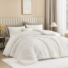 a bed with white comforter and pillows in a bedroom next to a lamp on a table