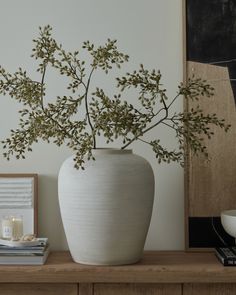 a white vase sitting on top of a wooden table next to a candle and other items