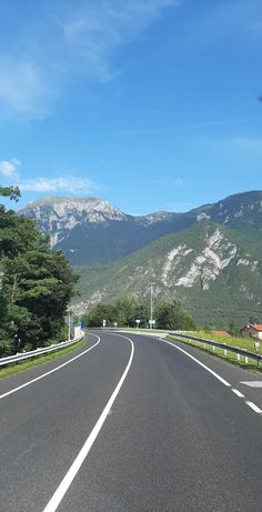 an empty road in the middle of mountains with trees on both sides and blue sky above