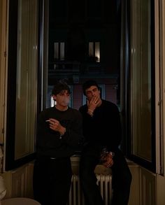 two men sitting next to each other on a window sill in front of a radiator