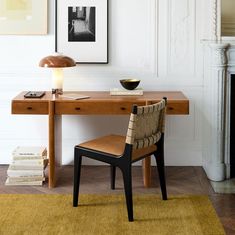 a wooden desk topped with a chair next to a lamp and pictures on the wall