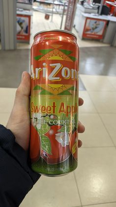 a person holding up a can of sweet apple juice in a grocery store's aisle