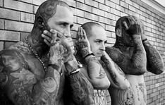 two tattooed men standing next to each other talking on their cell phones in front of a brick wall