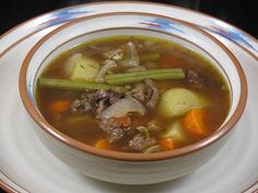 a bowl of soup with meat, potatoes and carrots