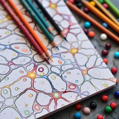 colored pencils and markers are on top of a coloring book with an abstract design