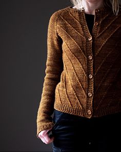 a woman wearing a brown cardigan standing in front of a dark background with her hands on her hips