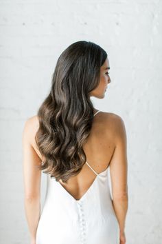 the back of a woman's head with long, wavy hair in front of a white wall