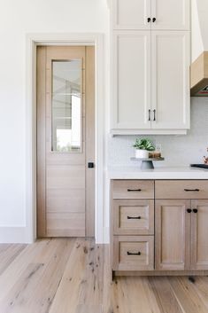 a kitchen with white cabinets and wood floors in front of a door that leads to another room