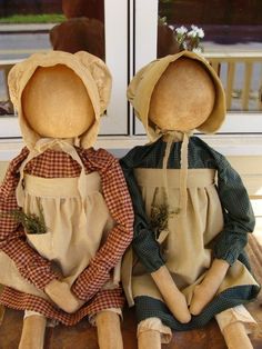 two cloth dolls sitting on top of a wooden table in front of a window,