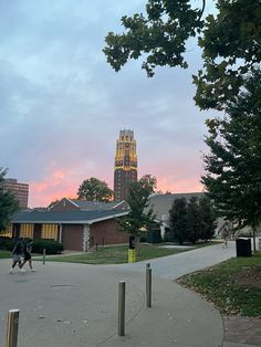 two people are walking down the sidewalk in front of a building with a clock tower