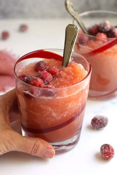 two glasses filled with fruit and ice cream on top of a white table next to cranberries