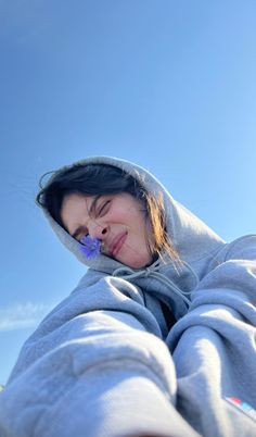 a woman wearing a gray hoodie holding a purple flower in her mouth and looking up into the sky