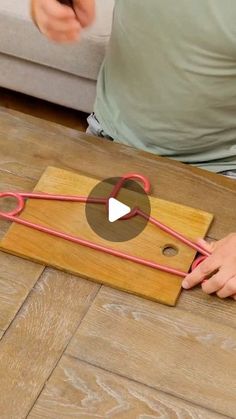 a person sitting on the floor with scissors in front of them and a piece of wood that has red string attached to it