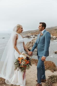 a bride and groom holding hands on the beach