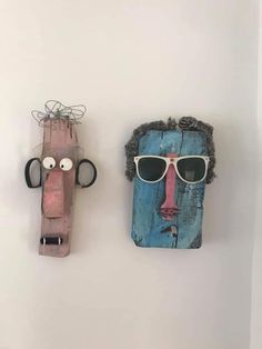 two wooden masks are hanging on the wall, one has sunglasses and the other has a face