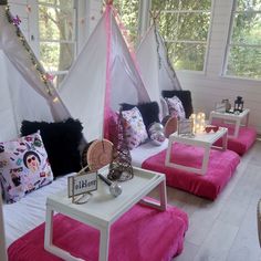 a living room filled with lots of furniture and pillows on top of pink blankets next to windows