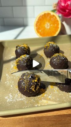 chocolate covered oranges on a baking sheet with a knife and flower in the background