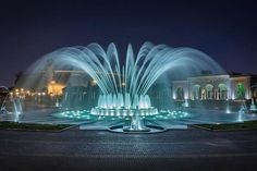 an illuminated fountain in the middle of a park at night with lights on it's sides