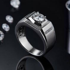 a white gold ring with two diamonds on it and some other jewelry items in the background